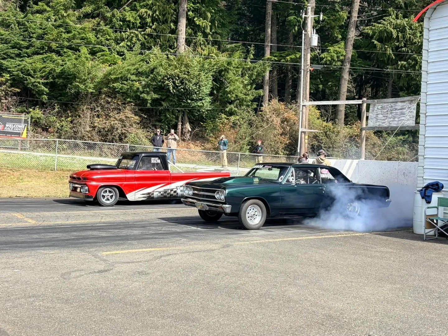 Two muscle cars smoking their tires side by side at the drag strip